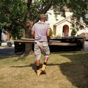 A Junk Unlimited Junk Removal worker carrying wooden planks towards a large dumpster in Laurel, MD.