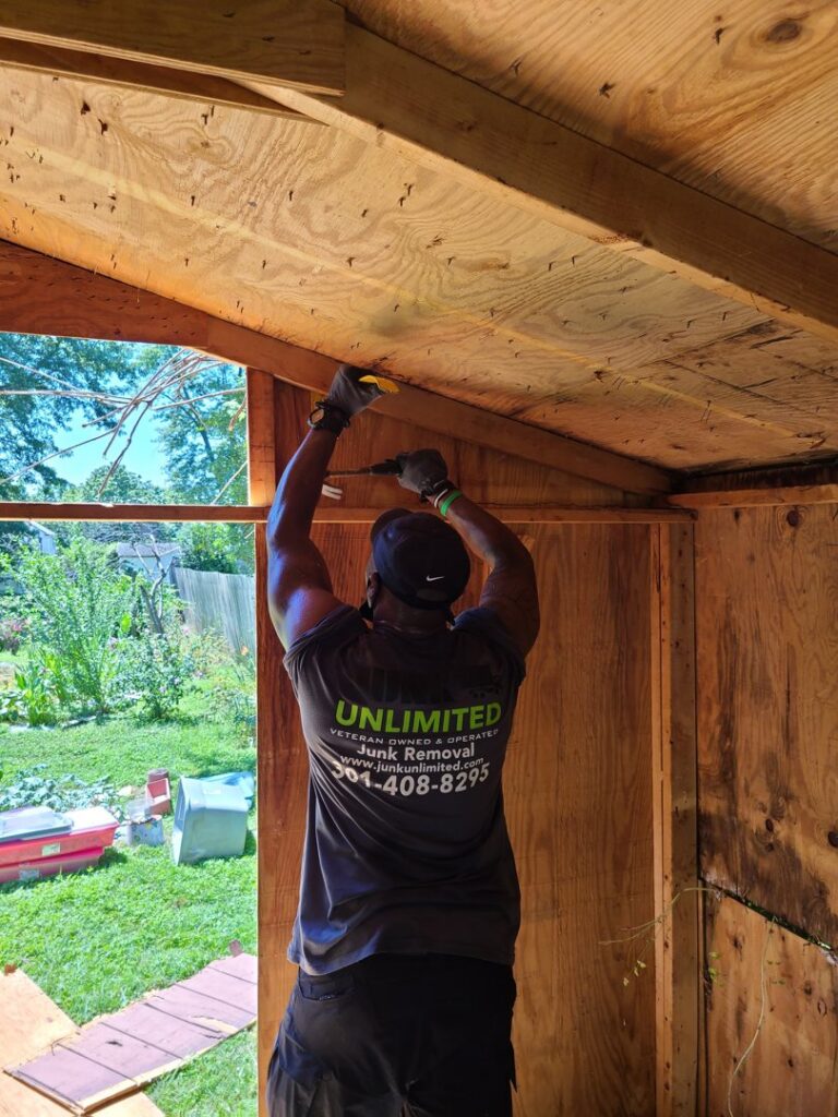 A Junk Unlimited Junk Removal worker dismantling the roof of a wooden shed as part of a junk removal service in Laurel, MD.