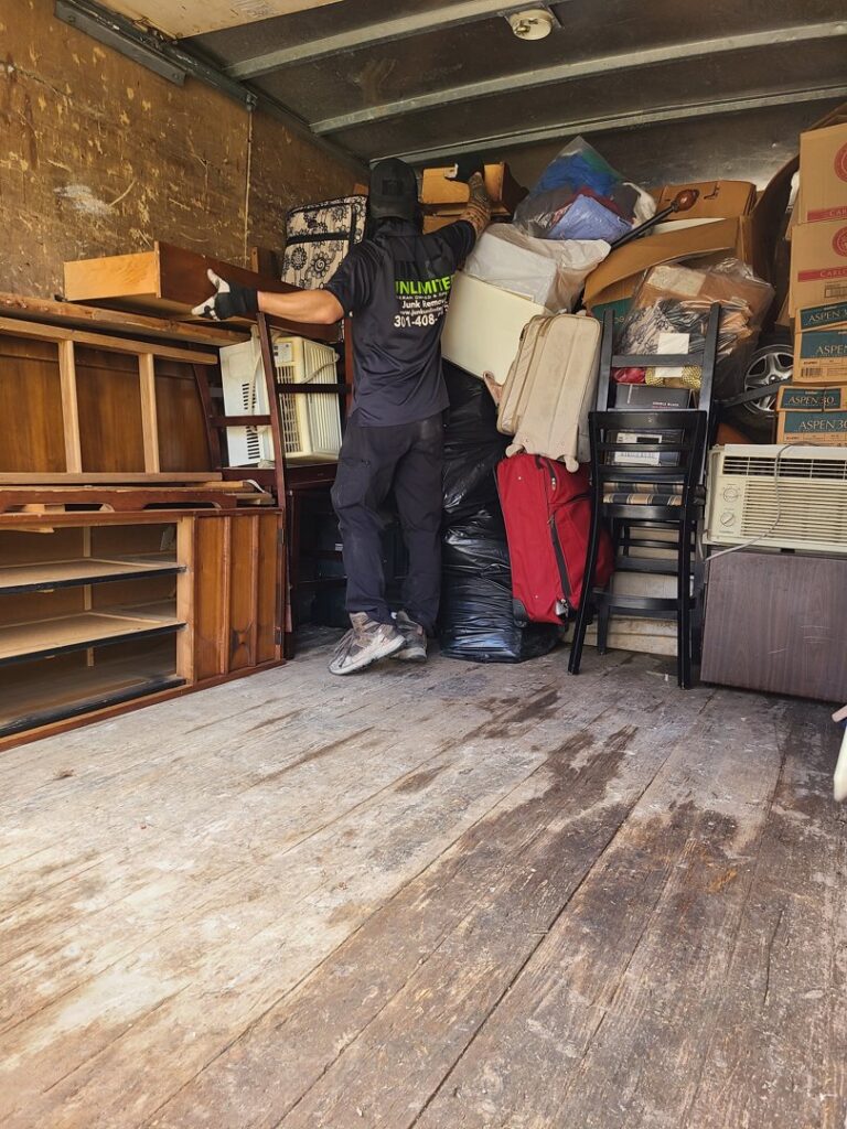 A Junk Unlimited Junk Removal worker loading various household items and furniture into a truck in Laurel, MD.