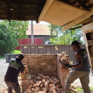 Two Junk Unlimited Junk Removal workers actively demolishing a brick structure, creating debris for removal in Laurel, MD.