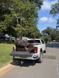 A Junkjet pickup truck hauling a large brown armchair on a residential street in Charlotte, NC.