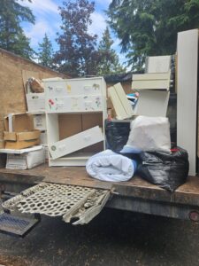 A Junkzilla Inc. truck loaded with a dresser, cardboard boxes, and black trash bags for removal in Everett, WA.