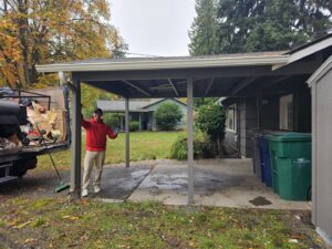 A Junkzilla Inc. worker giving a thumbs-up next to a partially loaded junk removal truck at a residential carport in Everett, WA.