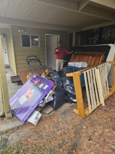 A Junkzilla Inc. worker removing large items, mattresses, and trash bags from a covered patio area in Everett, WA.