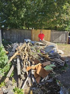 A Junkzilla Inc. worker standing next to a large pile of yard waste and wood debris in a backyard in Everett, WA.