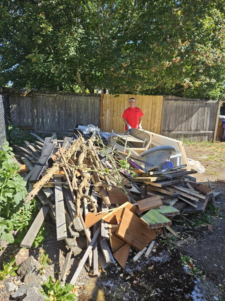 A Junkzilla Inc. worker standing next to a large pile of yard waste and wood debris in a backyard in Everett, WA.