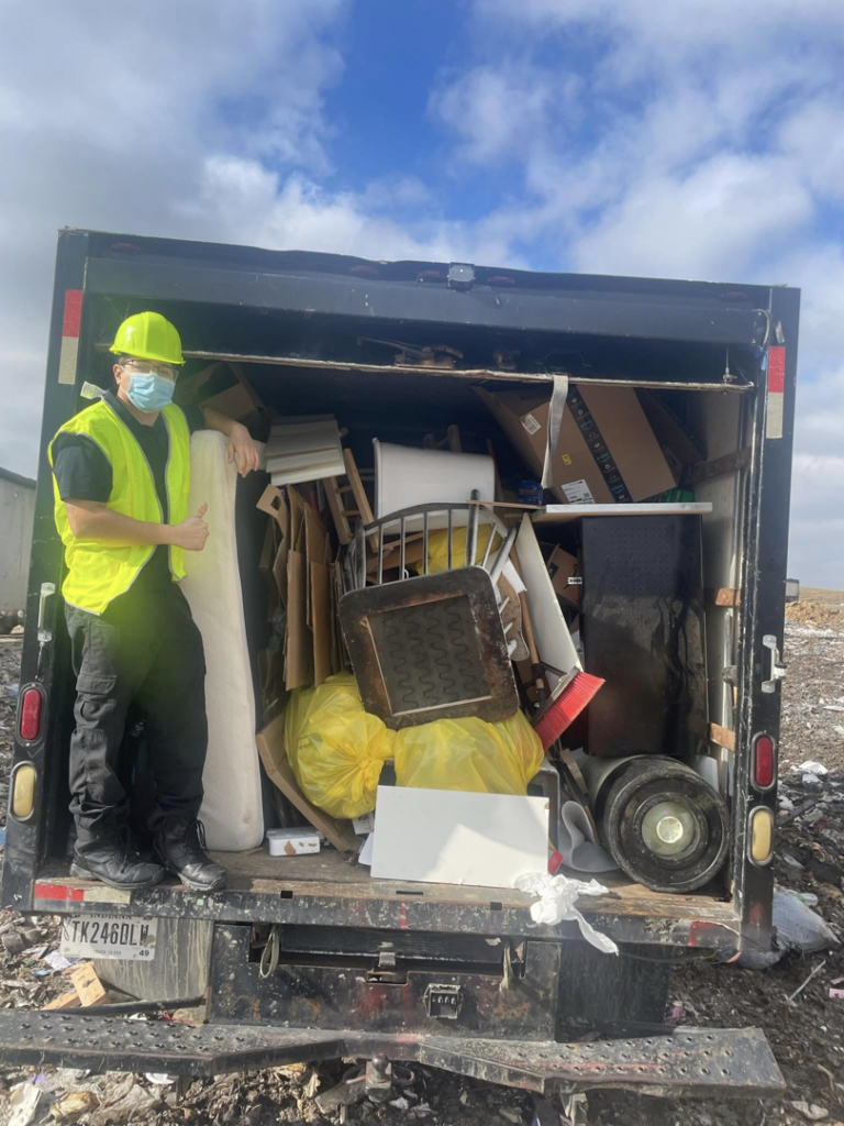 A Junkzilla worker in safety gear stands proudly next to a full junk removal truck in Indianapolis, IN, ready for disposal.