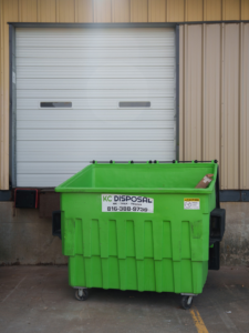A green KC Disposal commercial dumpster placed in front of a loading dock in Kansas City, KS.