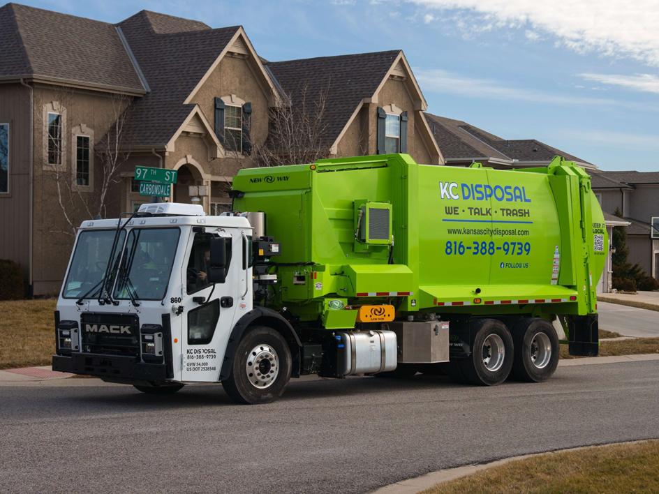 A bright green KC Disposal garbage truck on a residential street in Kansas City, KS, ready for junk removal service.