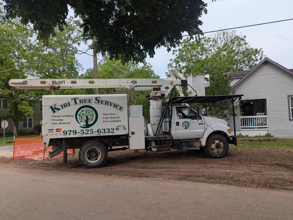 A KIRI TREE service bucket truck with company logo and contact information parked on a dirt road in Austin, TX.