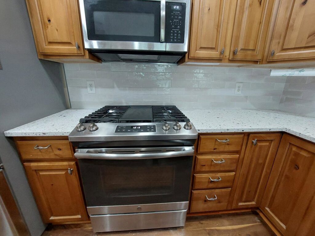 A renovated kitchen featuring new stainless steel appliances, a tile backsplash, and updated countertops by Jake and Jake Construction LLC in Sandy, UT.