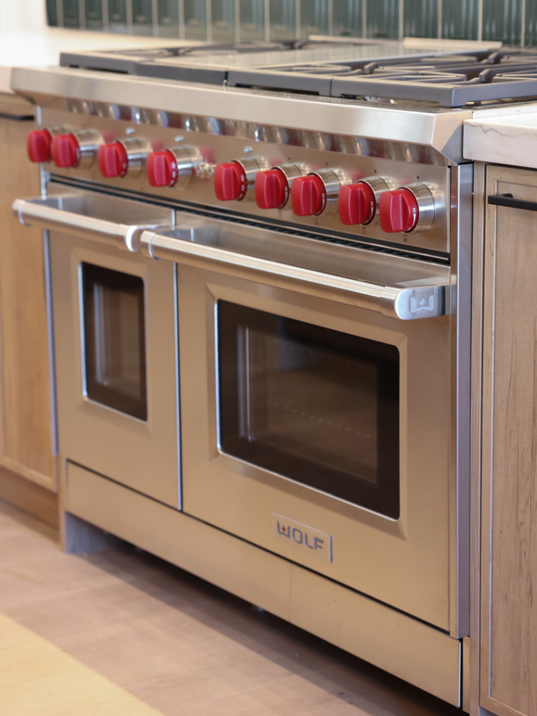 A professional installation of a stainless steel Wolf range with red knobs in a modern kitchen by Ella Lee Homes in Scottsdale, AZ.