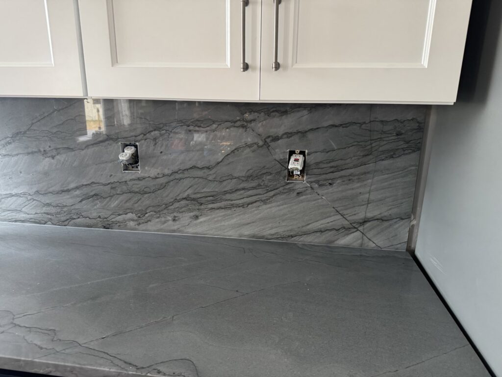 A newly installed kitchen backsplash with exposed electrical outlets by Victor's Granite Counter-Tops in Millcreek, UT.