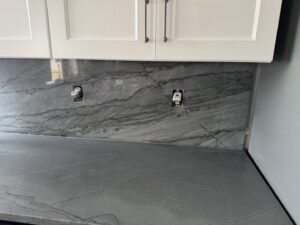 A newly installed kitchen backsplash with exposed electrical outlets by Victor's Granite Counter-Tops in Millcreek, UT.