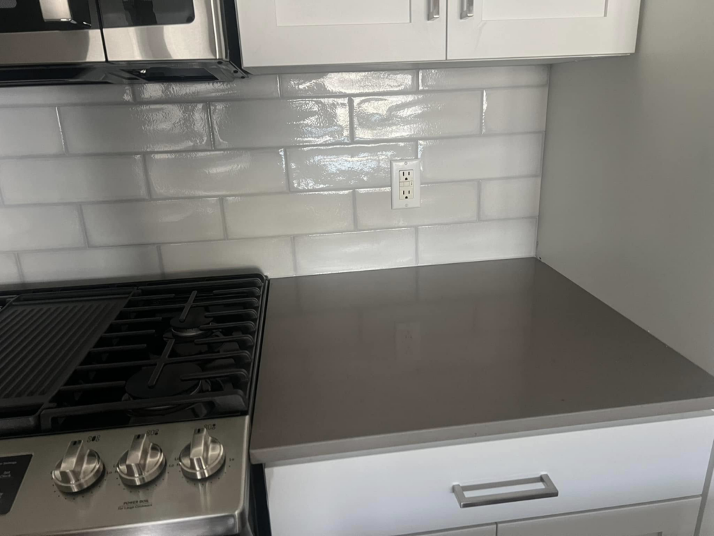 Detailed view of a kitchen backsplash and countertop installation near a stove and microwave by Fox Solutions Corp in Worcester, MA