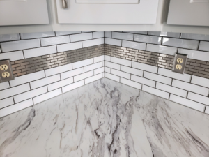 A newly installed kitchen backsplash with white subway tiles and a metallic accent strip by Bryan's Home Services in Fargo, ND.