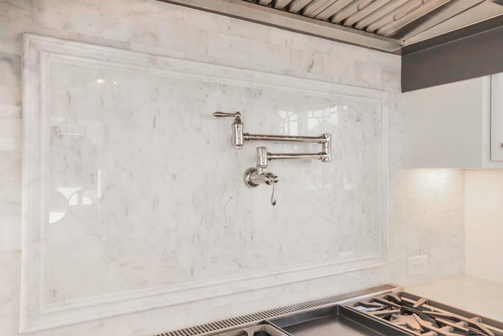 A newly installed kitchen backsplash with decorative tile and a pot filler faucet by Traditions Construction, LLC in Baton Rouge, LA.