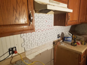 A kitchen wall with geometric backsplash tiles partially installed, showing a remodeling project by Clayton's Remodeling And Home Services in Vero Beach, FL.