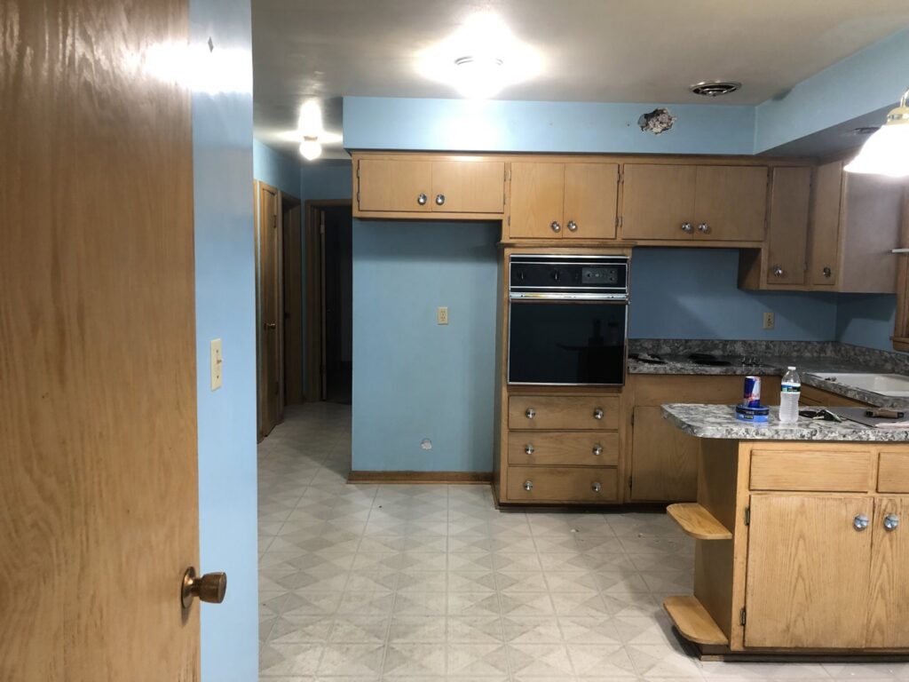 A kitchen before a remodel, showing old cabinets, blue walls, and dated flooring by RT Property Services in Allendale, MI
