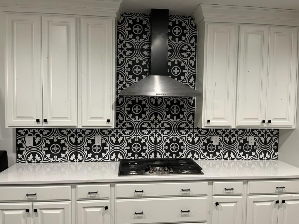 A modern kitchen featuring new white cabinets, a range hood, and a decorative black and white tiled backsplash installed by Joel's Handyman in Ogden, UT.