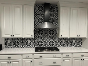 A modern kitchen featuring new white cabinets, a range hood, and a decorative black and white tiled backsplash installed by Joel's Handyman in Ogden, UT.
