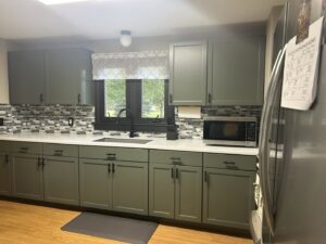 A newly renovated kitchen with green cabinets, white countertops, and a stylish tiled backsplash by Prime Construction And Flooring in Lorain, OH.