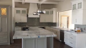 A kitchen featuring new white cabinets, grey backsplash, and a large island installed by Dahlman Construction in San Tan Valley, AZ.
