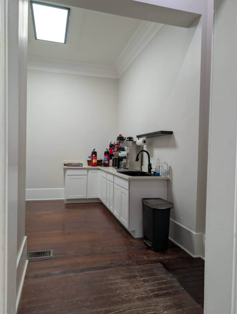 Newly installed white kitchen cabinets, countertop, and sink in a breakroom by Bourque's Quality Construction, LLC in Lafayette, LA.