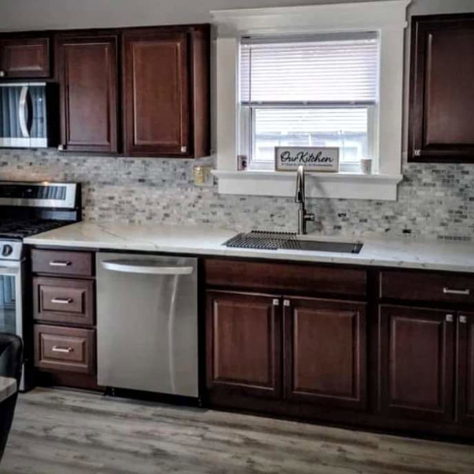 A renovated kitchen featuring dark wood cabinets, new countertops, and a tiled backsplash by Prime Construction And Flooring in Lorain, OH.