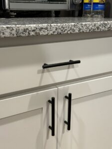 Close-up of newly installed black cabinet handles on white kitchen cabinets by Shore Home Construction Roofing in Salisbury, MD.
