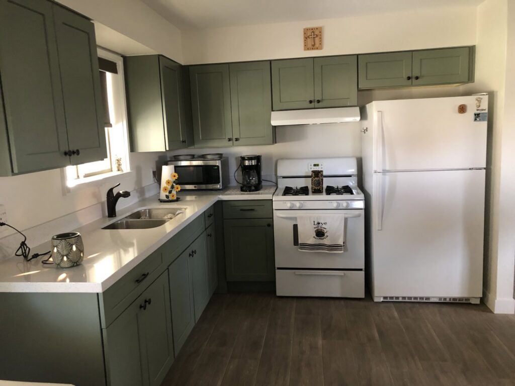 A kitchen featuring newly installed green cabinets and white countertops by Centennial Builders, LLC in Litchfield Park, AZ.