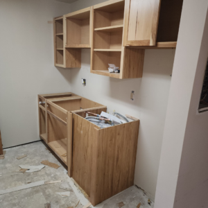 New wooden kitchen cabinets being installed by Excalibur Home Services in Council Bluffs, IA, showing plumbing and electrical rough-ins.