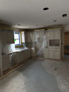 Kitchen cabinet installation in progress with cabinets protected by plastic sheeting by Le Roux Homes in Enid, OK.