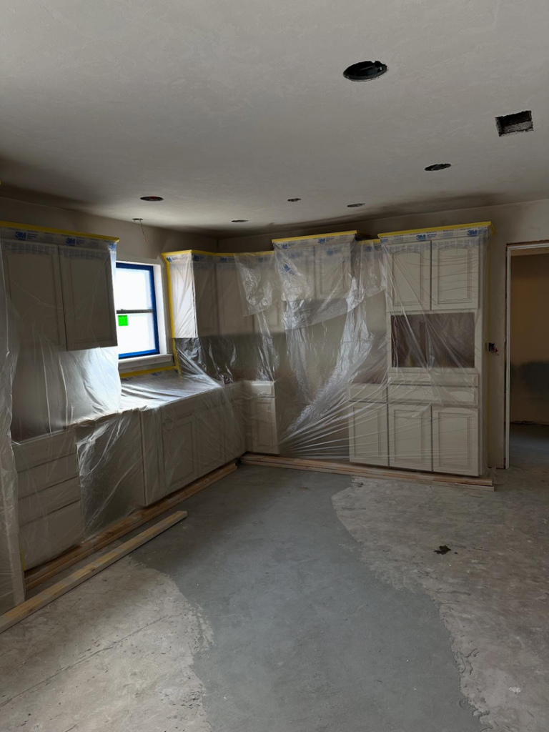 Kitchen cabinet installation in progress with cabinets protected by plastic sheeting by Le Roux Homes in Enid, OK.