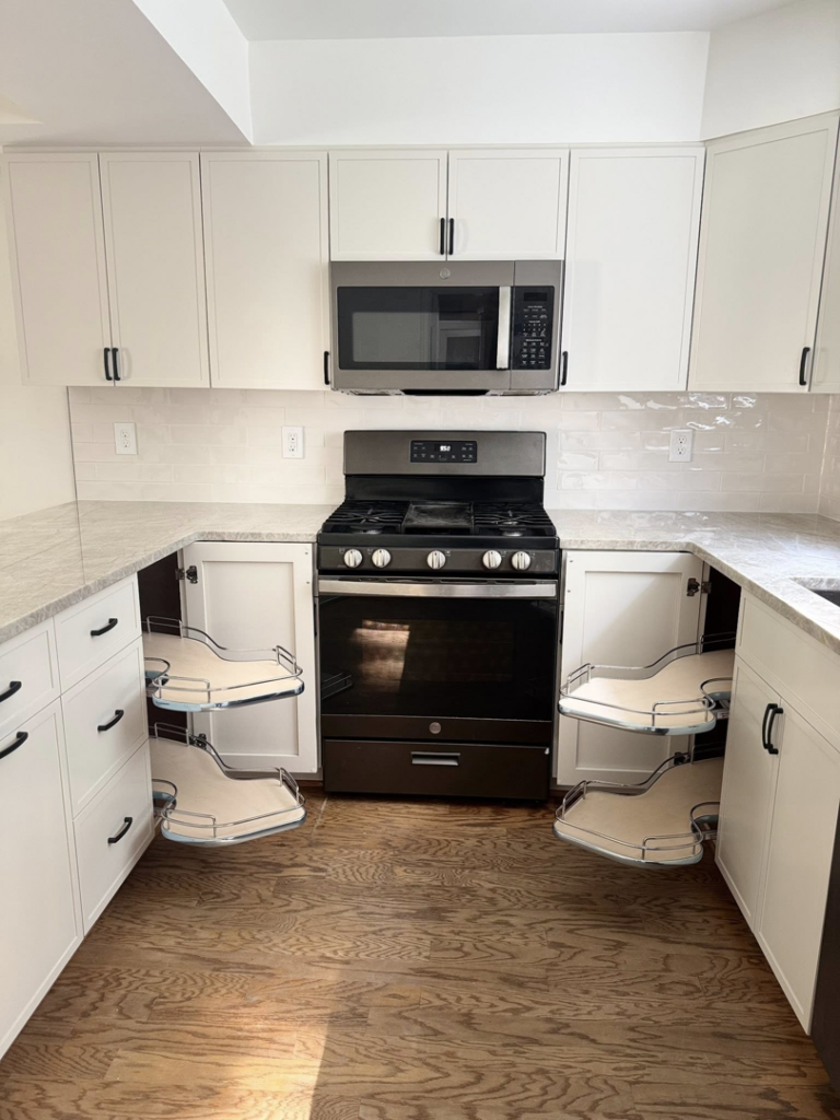 A newly installed kitchen with white custom cabinets, granite countertops, a gas range, microwave, and pull-out corner shelves by NC Home Remodeling and Custom Cabinetry in Alexandria, VA.