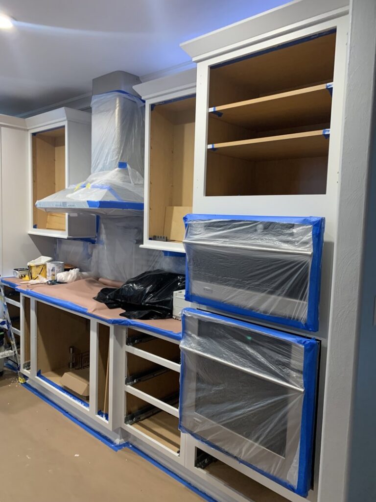 Kitchen cabinets taped and prepped for painting during a renovation project by Coastal Surface Design in Virginia Beach, VA.