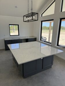 A kitchen construction in progress with dark gray cabinets and a large white island by Stone Age Granite of Austin, TX.