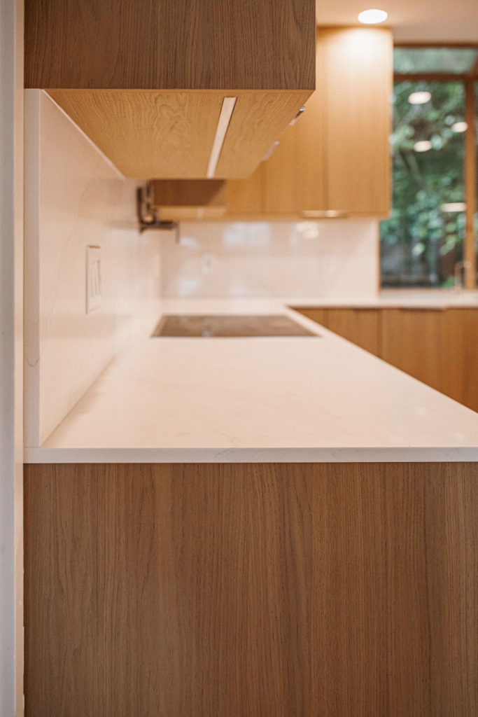 Side view of a newly installed kitchen counter with light wood cabinets and white backsplash by Atlantic Tile & Granite in Kent, WA.