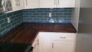Newly installed kitchen countertop with dark wood finish and teal subway tile backsplash by ALKA Construction/ Handyman Services in Layton, UT