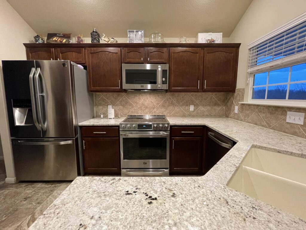 A kitchen remodel featuring dark wood cabinets, speckled light countertops, and stainless steel appliances by AAA Countertops in Austin, TX.