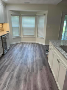 A renovated kitchen and dining area featuring new grey flooring and white cabinets by Nailed It Custom Remodeling in Chesapeake, VA.