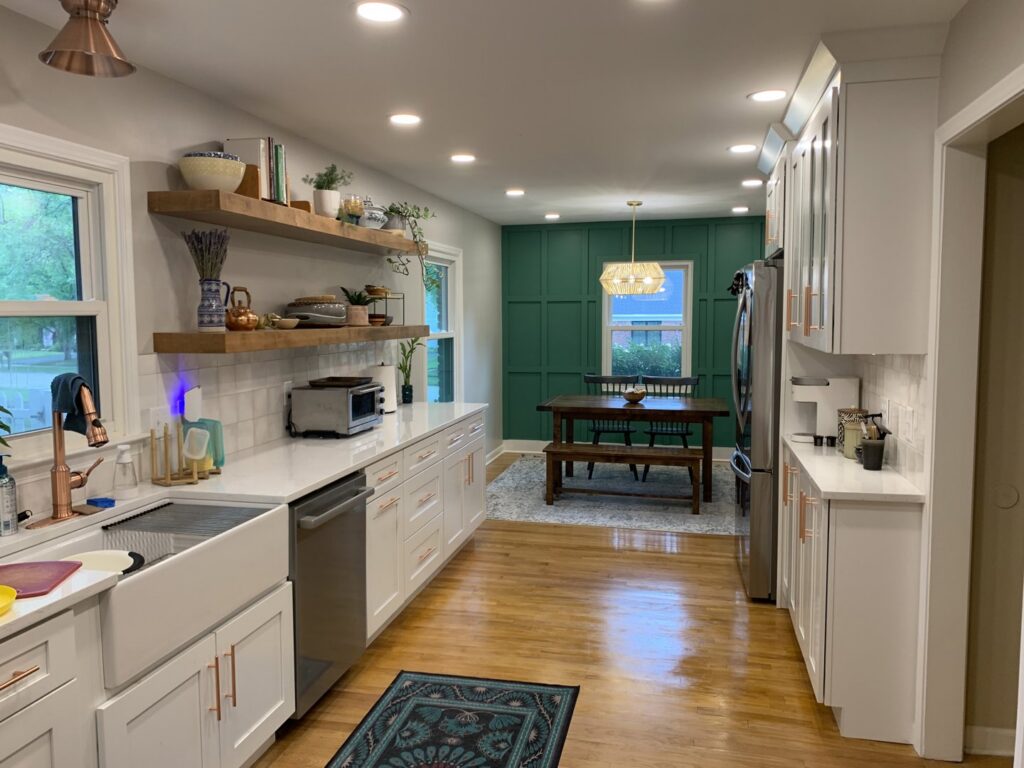 A kitchen and dining area remodel with white cabinets, open shelving, and a green accent wall by Benjamin Design - Build in Fishers, IN.