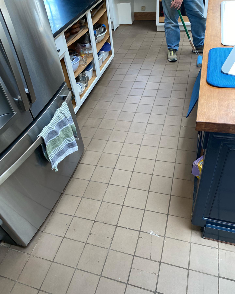 A handyman performing floor maintenance on light brown square kitchen tiles for Infinite Construction LLC in Bristol, CT.