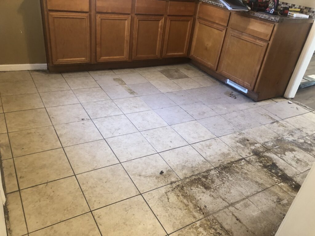 Kitchen floor during renovation with old tiles being removed, exposing the subfloor by RT Property Services in Allendale, MI
