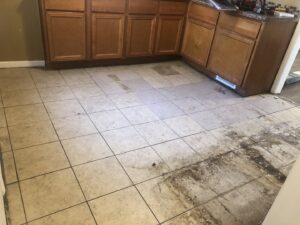Kitchen floor during renovation with old tiles being removed, exposing the subfloor by RT Property Services in Allendale, MI