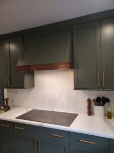 Kitchen featuring olive green cabinets, a custom wooden range hood, and white tile backsplash by Corkery Customs & Remodeling LLC in Philadelphia, PA
