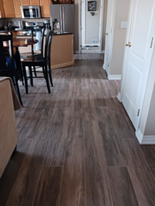A kitchen and adjacent hallway with newly installed wood-look tile flooring by Home Improvement Design Center in Ann Arbor, MI.