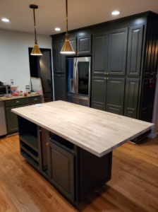 A newly installed kitchen island with a light wood countertop and dark green cabinets by Lilac Remodel Spokane in Spokane Valley, WA.
