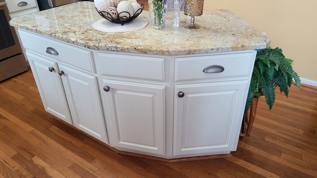 A kitchen island with freshly painted white cabinets and a granite countertop by Coastal Surface Design in Virginia Beach, VA.