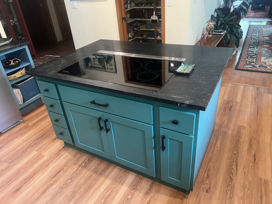 A custom kitchen island with a built-in cooktop and teal cabinets, installed by Prestige Statewide, LLC in Eugene, OR.